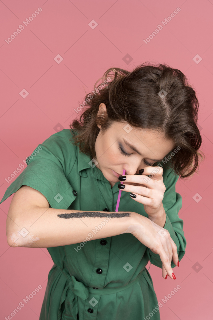 Woman inhaling black dust using pink straw
