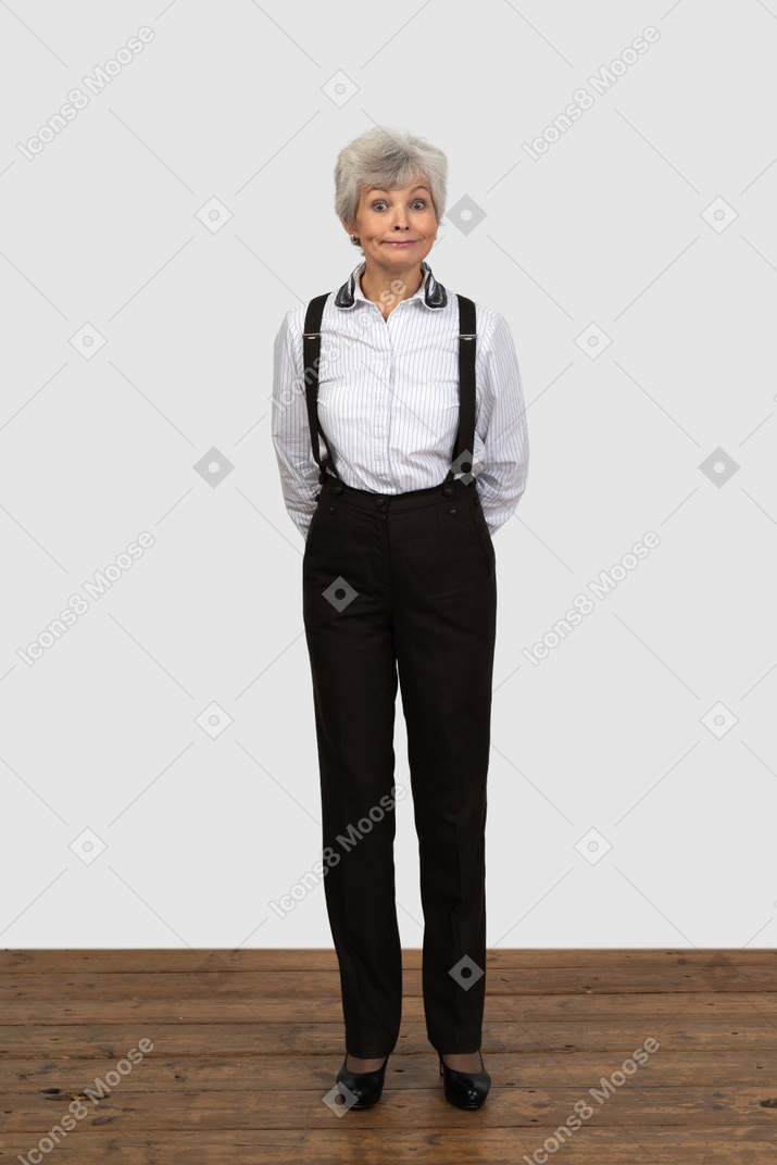一位不高兴的老妇在办公室的衣服，双手背后做鬼脸的前视图