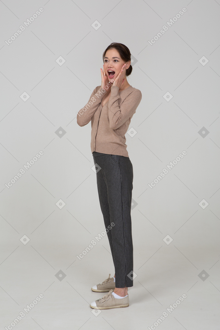 Three-quarter view of a pleased young lady in beige pullover touching her face