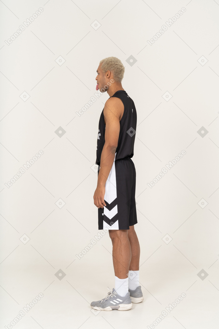 Vista posteriore di tre quarti di un giovane giocatore di basket maschile che mostra la lingua