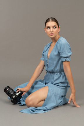 Side view of a young woman in blue dress sitting on a floor with camera