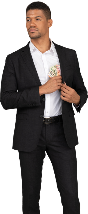 Вид спереди молодого человека в черном костюме, кладущего банкноты в карман