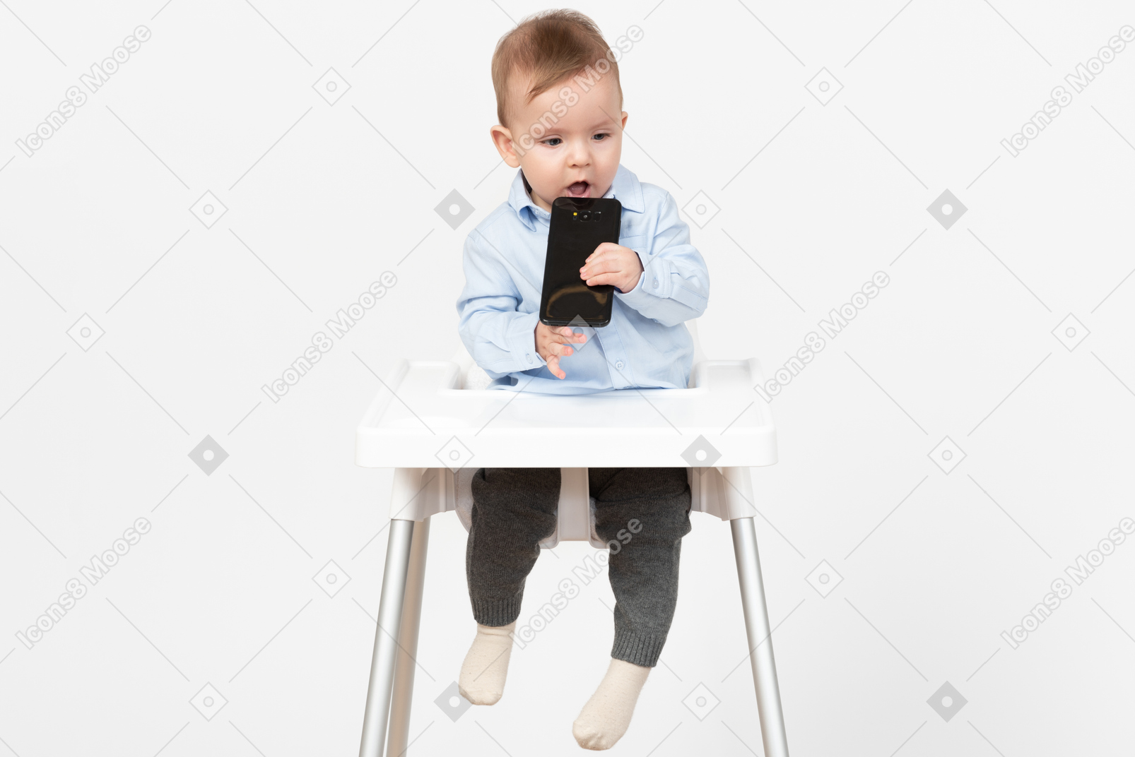Baby boy sitting in highchair and holding mobile phone