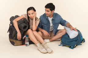 Jovem casal interracial sentado perto de mochilas enormes