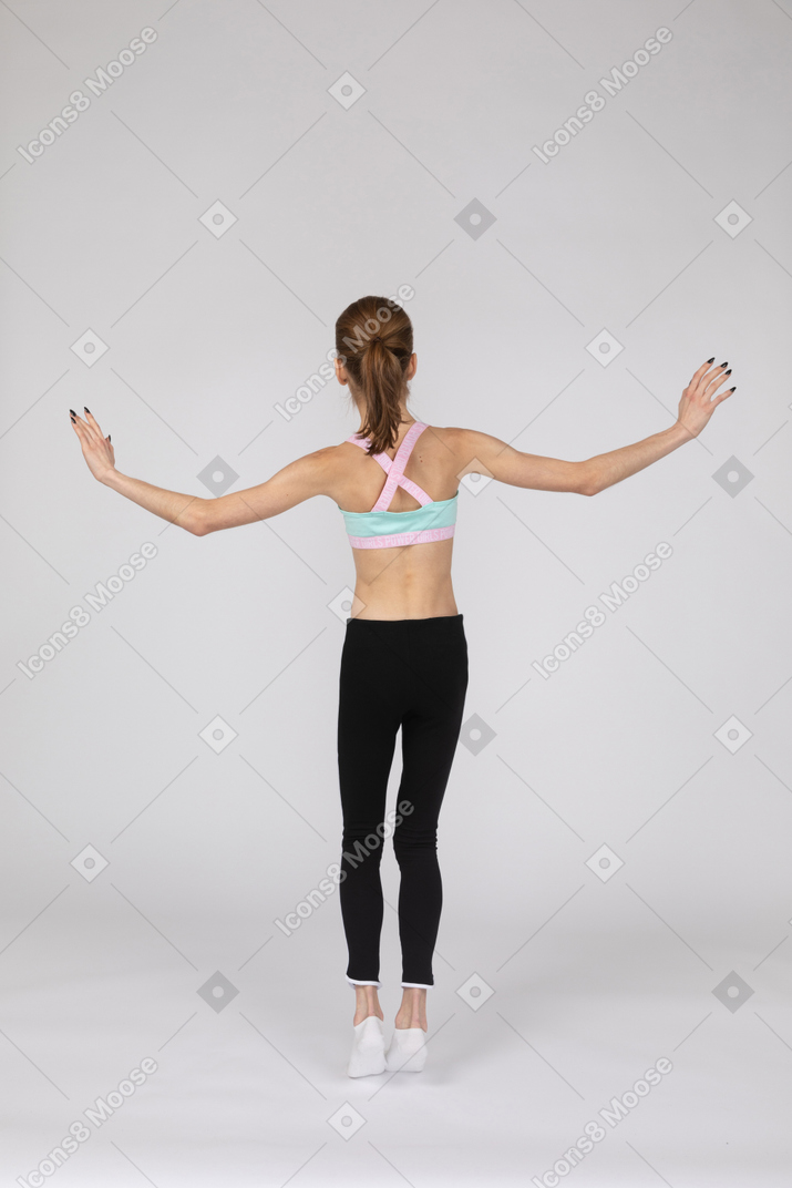 手を上げながらつま先でバランスをとるスポーツウェアの10代の少女の背面図