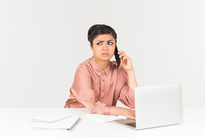 Надоело смотреть молодая индийская женщина разговаривает по телефону и работает на ноутбуке