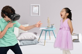 A little boy in virtual reality headset pointing imaginary gun at screaming girl