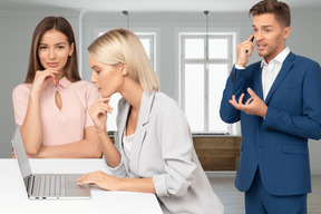 A couple of people that are standing in front of a laptop