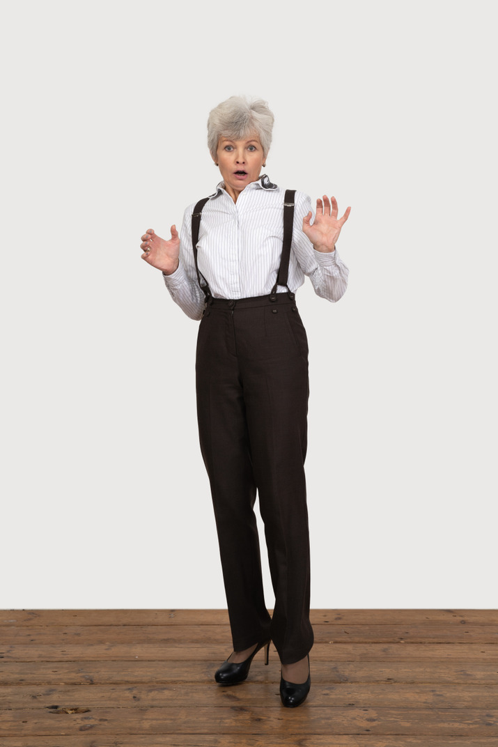 Front view of an astonished old lady raising and outspreading hands