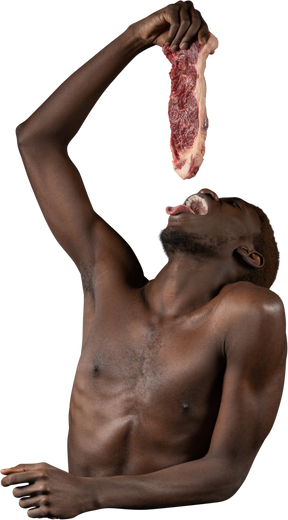 Vista frontale di un giovane afro che tiene una fetta di carne mentre apre la bocca
