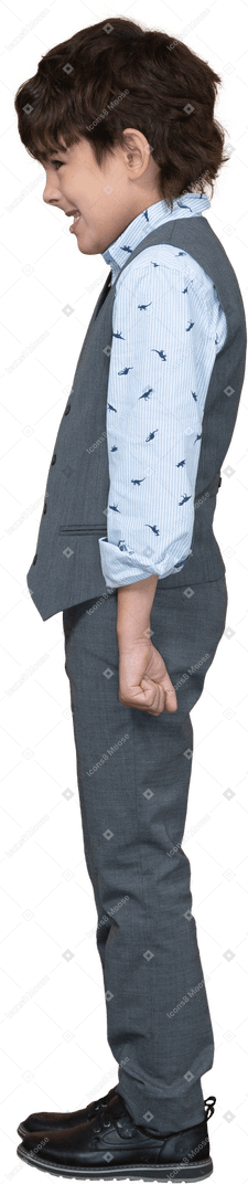 Vista lateral de um menino zangado em um terno cinza em pé com os punhos cerrados