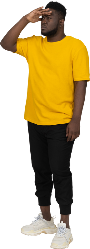何かを探している黄色のtシャツを着た若い浅黒い肌の男の4分の3のビュー