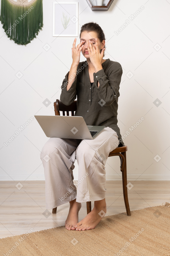 Three-quarter view of a busy young woman with a headache sitting on a chair with a laptop