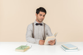 Joven profesor sentado en la mesa y leyendo un libro