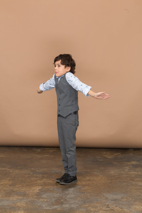Vista lateral de un niño con traje de pie con los brazos extendidos