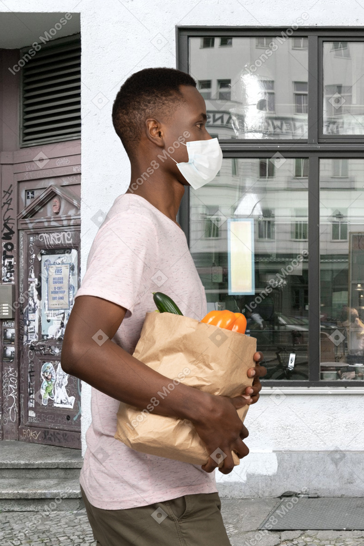 A man wearing a face mask holding a bag of groceries