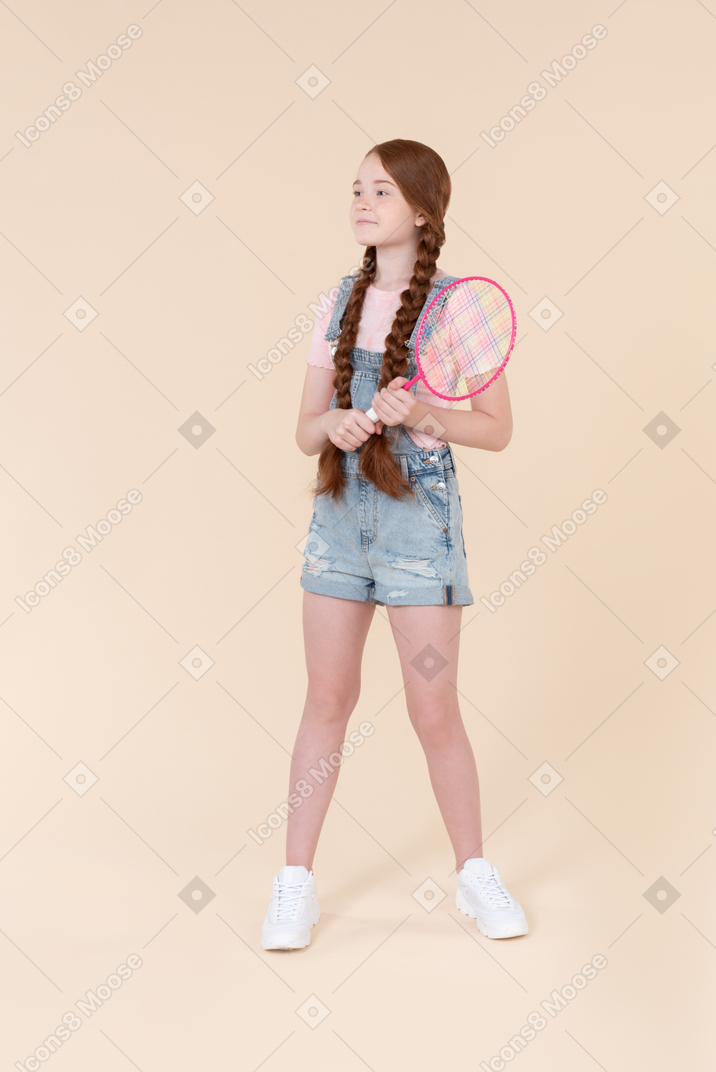Teenage girl holding tennis racket and standing back to camera