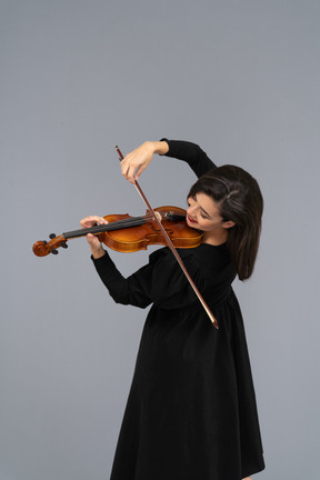 Close-up de uma jovem alegre de vestido preto tocando violino