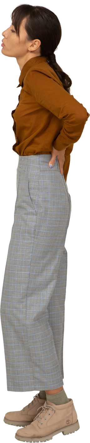 Vista lateral de uma jovem mulher asiática de calça e blusa tocando as costas