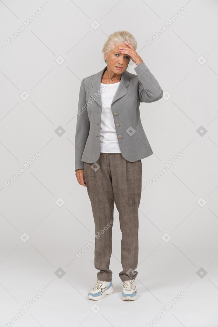 Front view of an old lady in suit touching her forehead