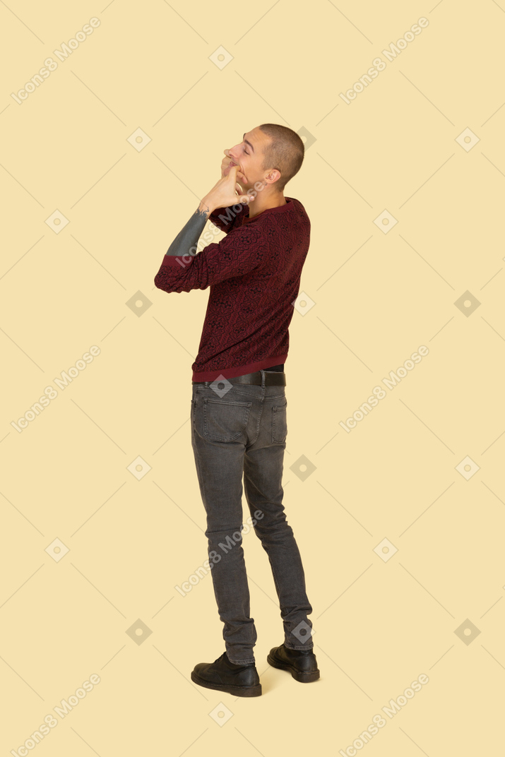 Vista traseira de três quartos de um jovem fazendo caretas tocando sua boca
