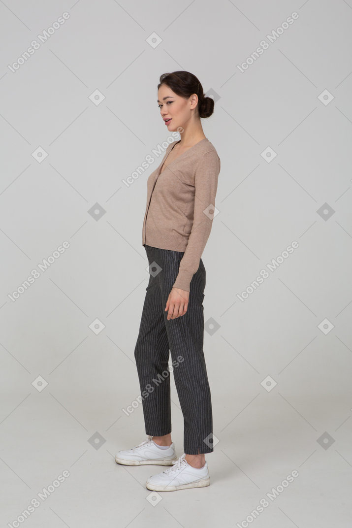 Three-quarter view of a sly young lady standing still in pullover and pants
