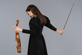 弓を作る黒いドレスを着た女性のバイオリン奏者の 4 分の 3 の後ろ姿