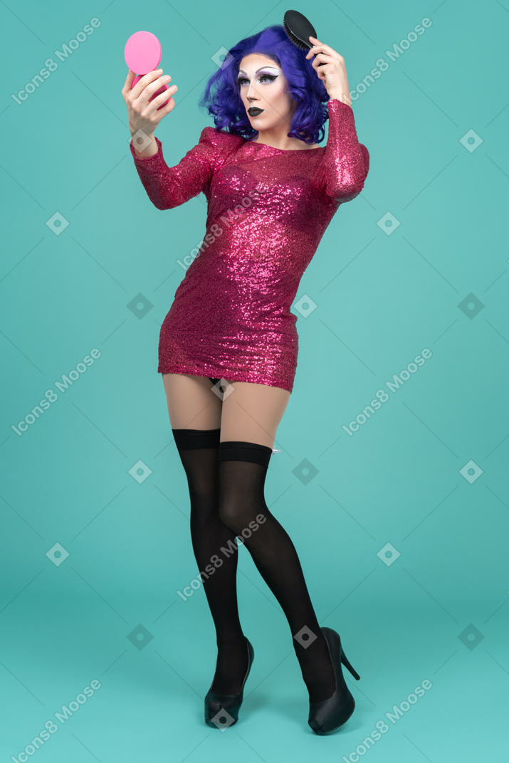 Drag queen in pink dress fixing their hair while looking in the mirror