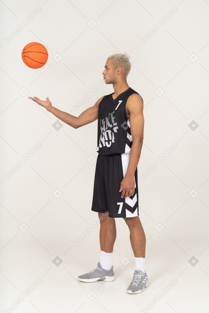 Vista de tres cuartos de un joven jugador de baloncesto masculino lanzando una pelota