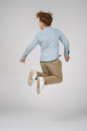 Back view of a boy in casual clothes jumping high in the air