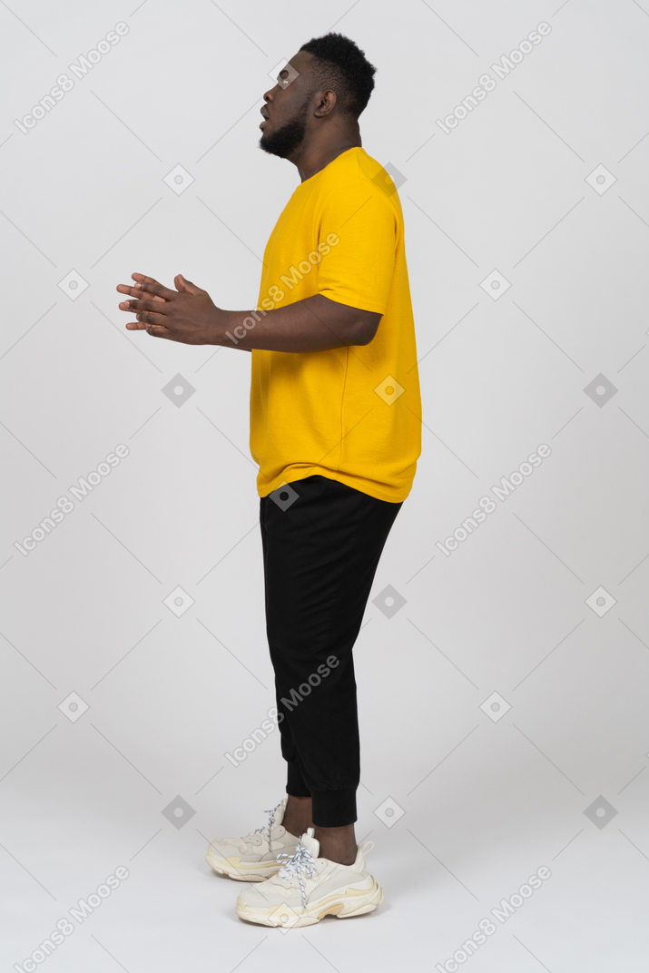 Vista lateral de un joven de piel oscura conmocionado en camiseta amarilla levantando las manos