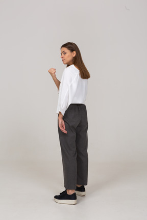 Three-quarter back view of an angry young lady in office clothing clenching fist