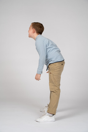 Vista lateral de un niño feliz agachándose y mirando a un lado
