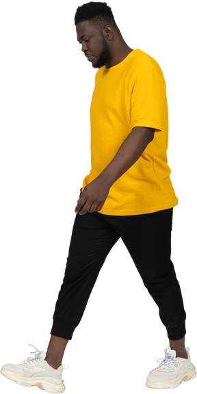 Vista de três quartos de um jovem de pele escura andando em uma camiseta amarela