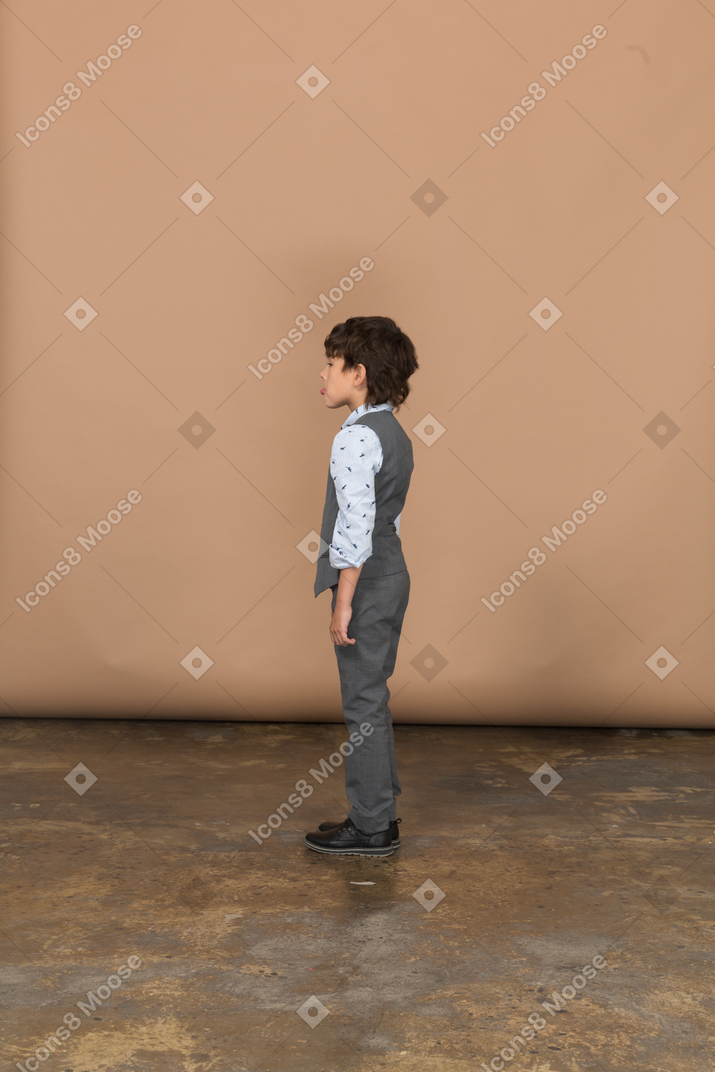Мальчик в сером костюме стоит в профиль