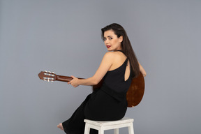 Bella donna che suona una chitarra mentre seduto metà si è rivolto a una macchina fotografica