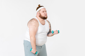 Tired big guy in sportswear lifting hand weights