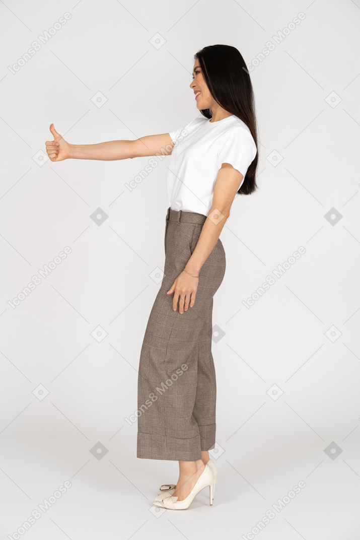 Вид сбоку улыбающейся молодой леди в бриджах и футболке, показывая большой палец вверх
