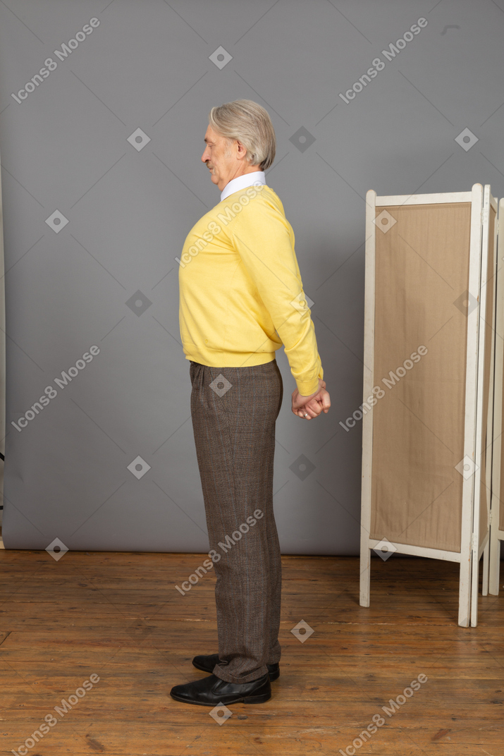 Side view of an old man stretching his back by holding hands behind