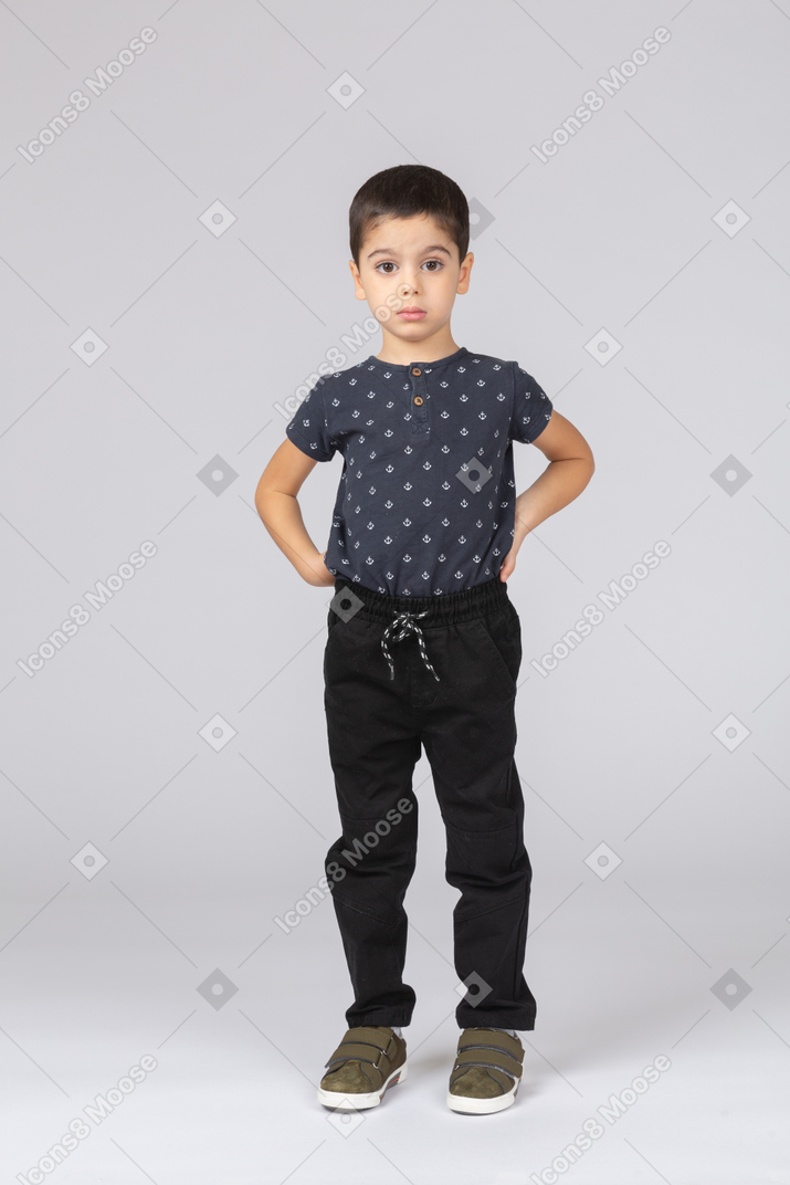 Vista frontal de un chico lindo en ropa casual posando con las manos en la espalda y mirando a la cámara