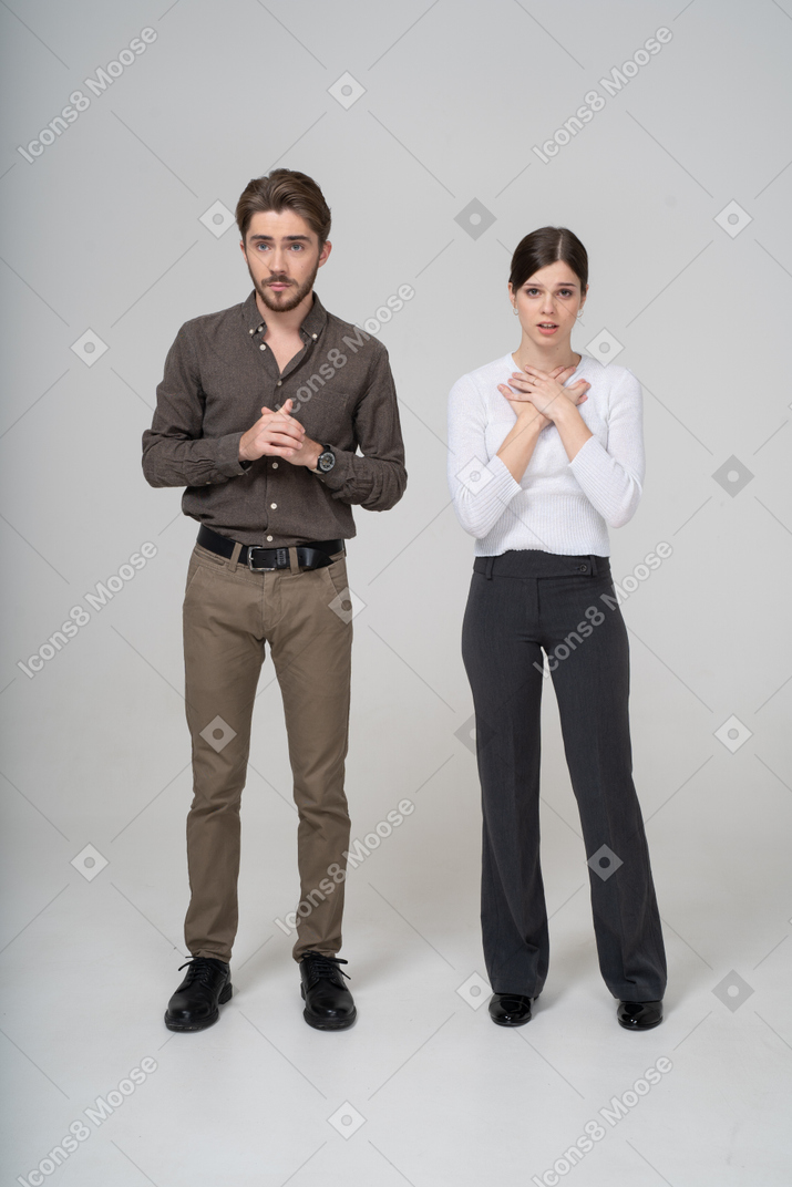 Front view of a worried young couple in office clothing holding hands together
