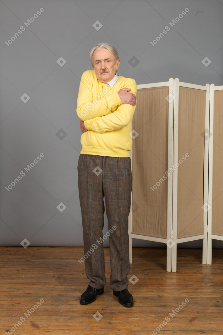 Vista lateral de un anciano sospechoso abrazándose a sí mismo