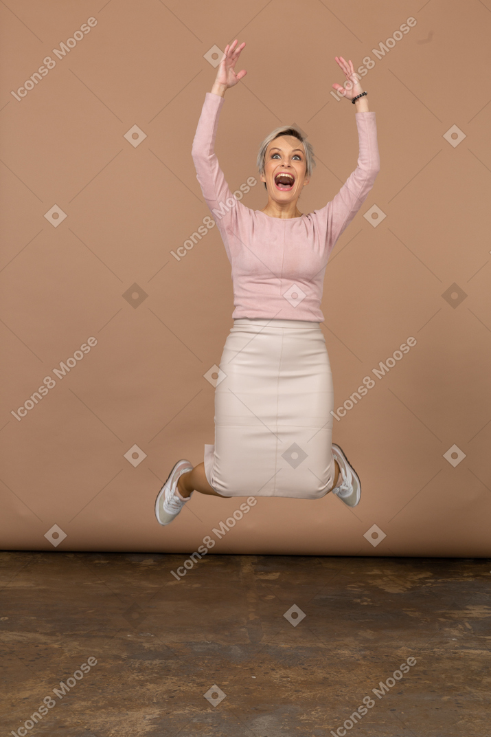 Front view of an emotional woman in casual clothes jumping with raised arms