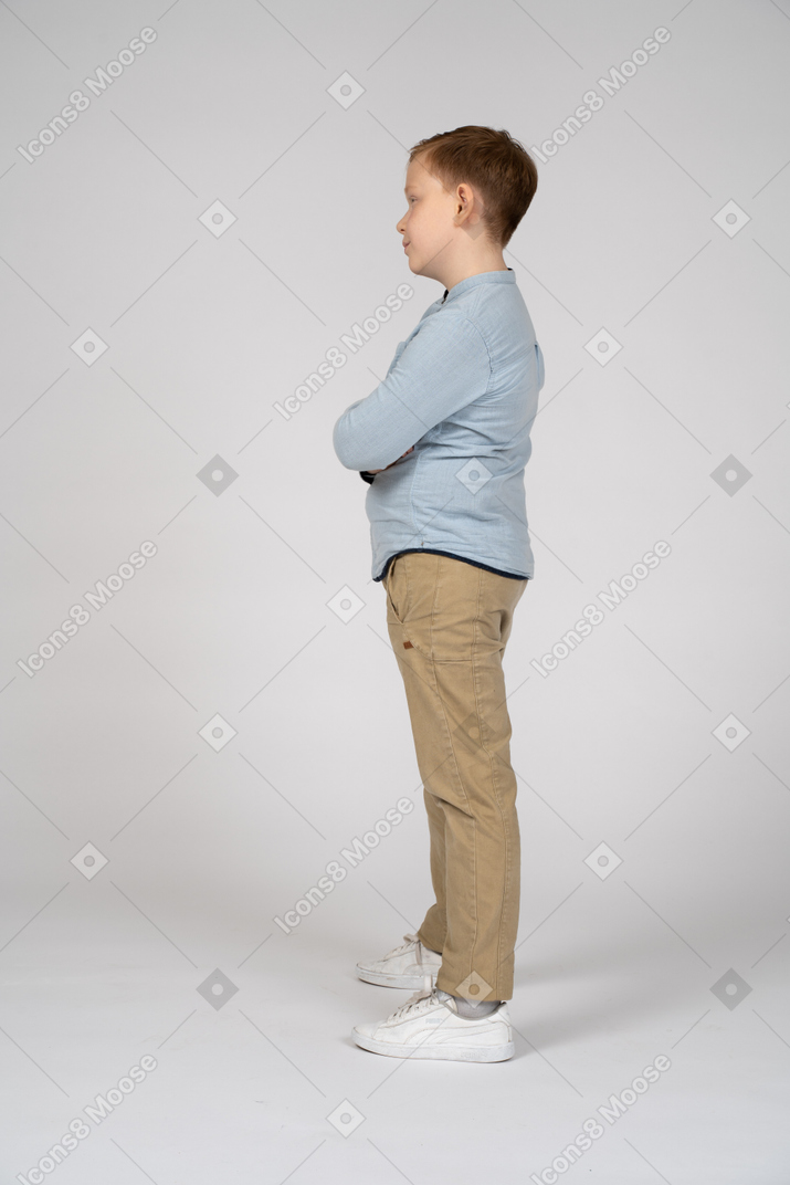 Vue latérale d'un garçon mignon debout avec les bras croisés