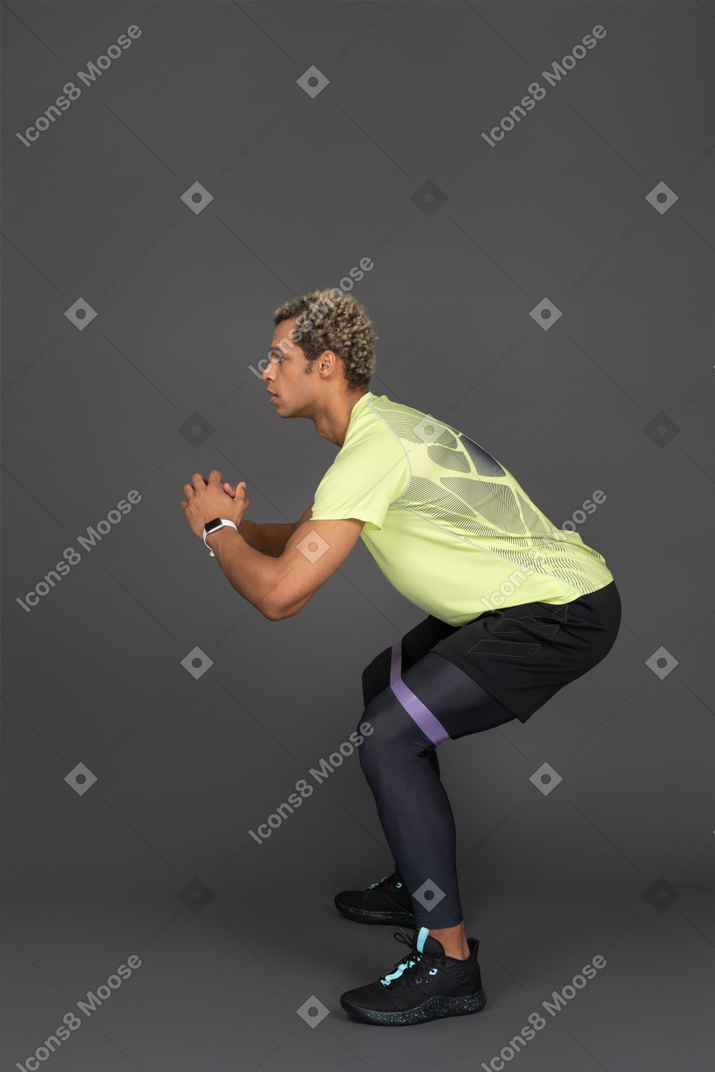 Side view of a dark-skinned young man squatting with an elastic rubber