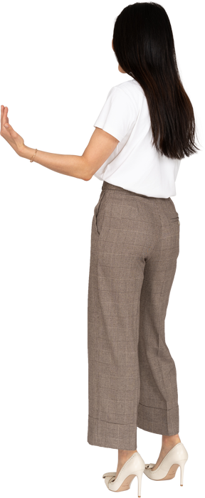 Vista posteriore di tre quarti di una giovane donna in calzoni che tende le mani