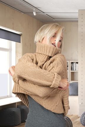 A woman in a sweater is standing by a window