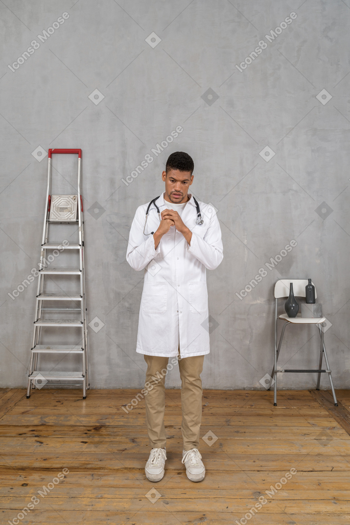 Вид спереди взволнованного молодого врача, стоящего в комнате с лестницей и стулом
