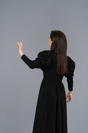 Back view of a young lady in a black dress raising her hand