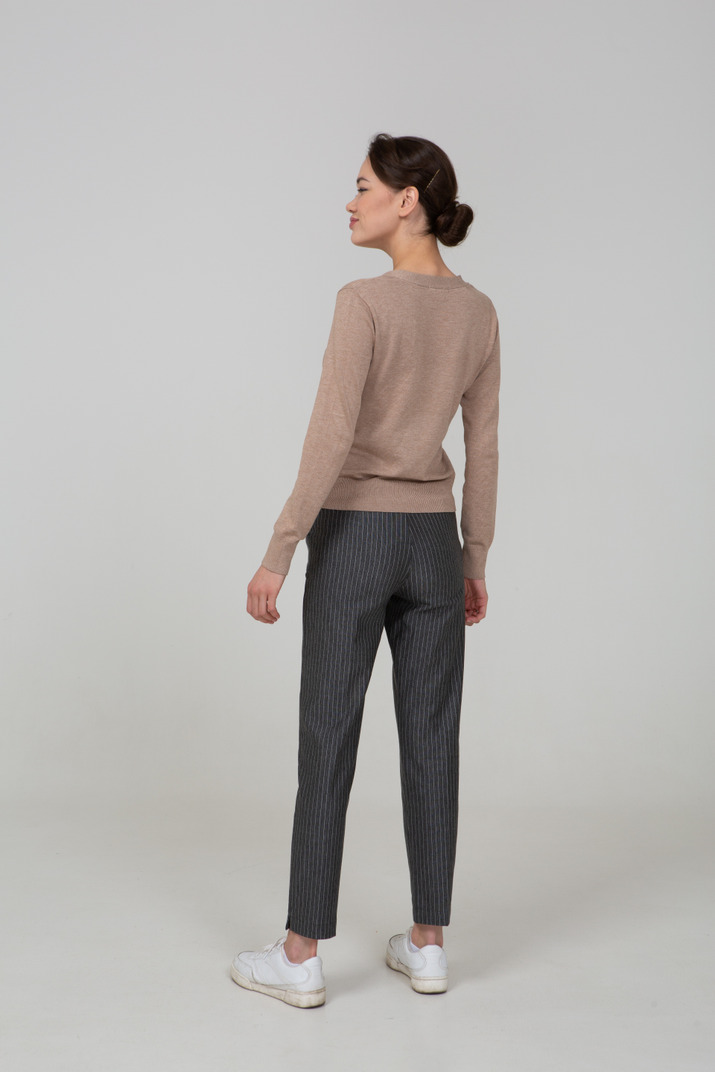 Three-quarter back view of a suspicious young lady in pullover and pants